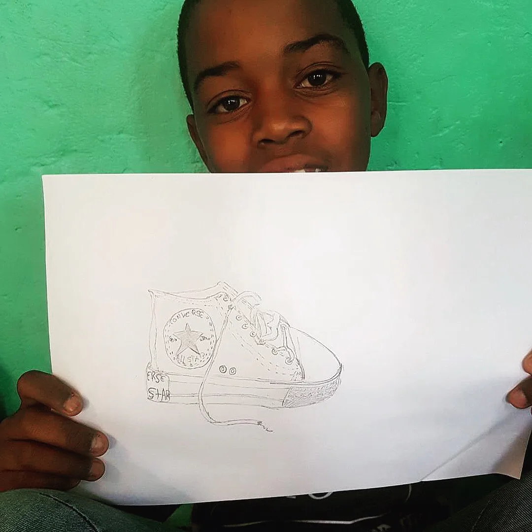 A learner holding up his pencil drawing of a sneaker